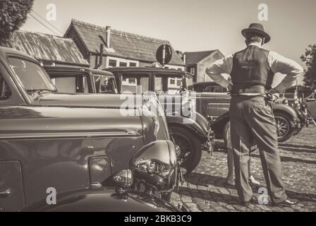 Vue arrière monochrome de 1940 personnes avec des voitures classiques d'époque garées à la station du patrimoine de Severn Valley Railway, événement d'été de la Seconde Guerre mondiale des années 1940, Royaume-Uni. Banque D'Images