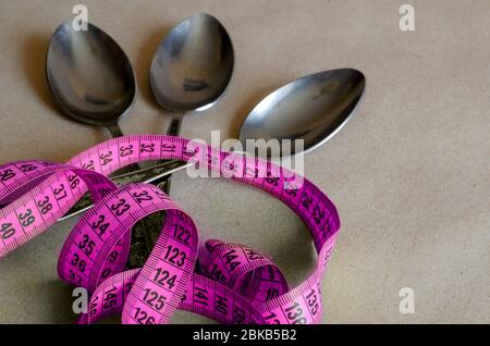 Tailleur et trois cuillères à soupe. Ruban de mesure sur trois cuillères à soupe métalliques. Le concept de la suralimentation pendant les problèmes psychologiques. . Sélectionnez Banque D'Images