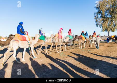 Groupe de touristes se préparer pour une promenade en chameau avec les longs vêtements traditionnels et la tête couvrant Marrakech, Maroc, Afrique du Nord Banque D'Images