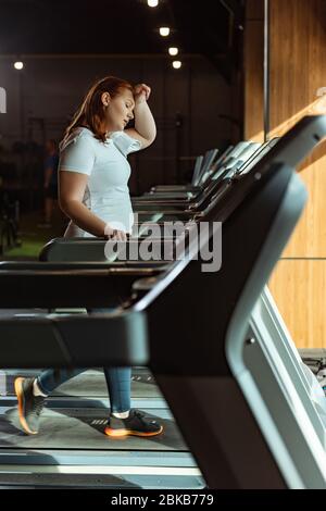 foyer sélectif de fille en surpoids fatiguée touchant le front pendant la course sur tapis roulant Banque D'Images