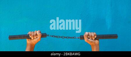 Tenue Nunchaku à la main isolée sur fond bleu. Formation nunchaku noir pour débutant. Équipement d'arts martiaux Hot Tactical Gear. Banque D'Images