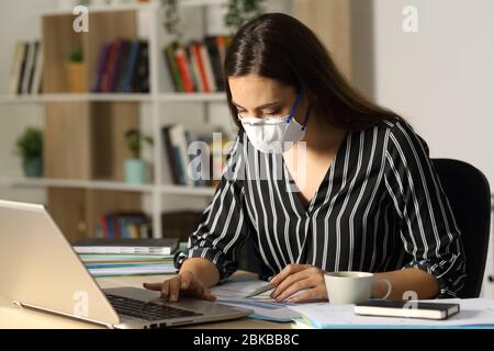 Femme d'entrepreneur comparant le rapport avec ordinateur portable évitant coronavirusavec masque assis sur un bureau à la maison de bureau la nuit Banque D'Images