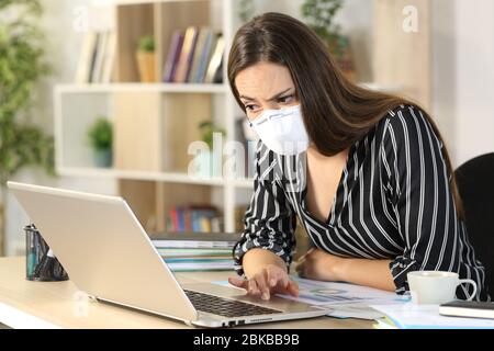 Une femme entrepreneure suspecte lisant de fausses nouvelles sur un ordinateur portable, assise sur un bureau à domicile Banque D'Images