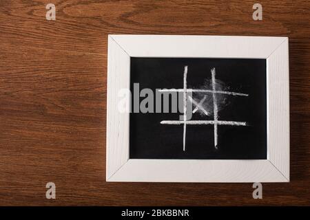 vue de dessus du jeu de l'orteil de tac tique sur le tableau noir avec grille de craie et croix sur la surface en bois Banque D'Images