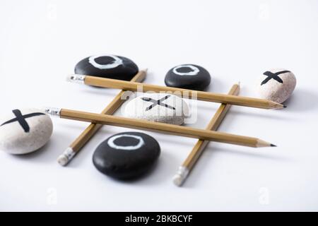 jeu de pieds tic tac avec grille faite de crayons et de galets marqués de naughts et de croix sur la surface blanche Banque D'Images