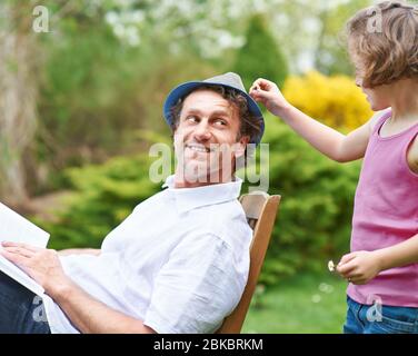 Une fille dans le jardin met une Marguerite sur le chapeau de son père Banque D'Images