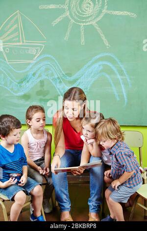 Les éducateurs et de nombreux enfants d'un groupe lisent un livre à la maternelle Banque D'Images