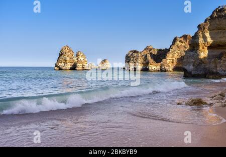 Falaises de la plage de Pinhao. Vue du dessous des vagues et sable vide au coucher du soleil. Concept de tourisme et de voyage sans croque. Algarve, Portugal Banque D'Images