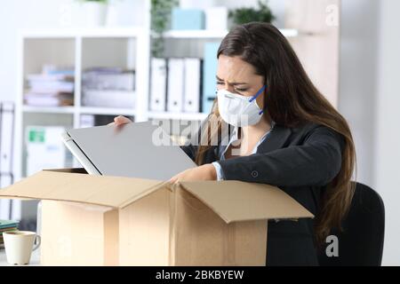 Triste a tiré la femme de la haute direction avec masque de protection pleurant son emballage sur une boîte au bureau Banque D'Images