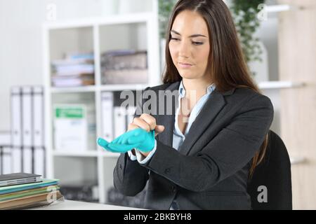 Femme exécutive sérieuse mettant des gants en latex évitant covid-19 assis sur un bureau Banque D'Images