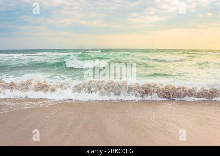 tempête sur la plage de sable au lever du soleil. paysage marin spectaculaire avec ciel nuageux. eau rugueuse et vagues en crash dans la lumière du matin Banque D'Images