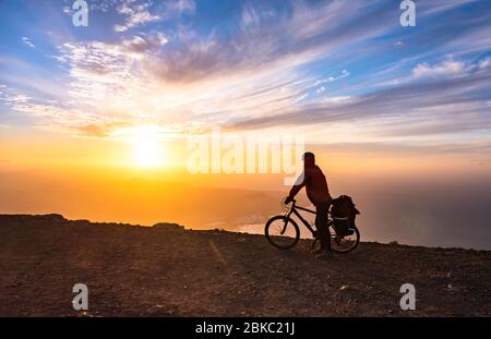 Mountain Bicycle Rider avec sac à dos voyage au-dessus de l'arrière-plan sunrise, Lanzarote Canary Island Banque D'Images