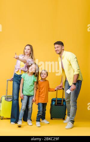 famille heureuse de voyageurs avec bagages, passeports et billets pointant sur le jaune Banque D'Images