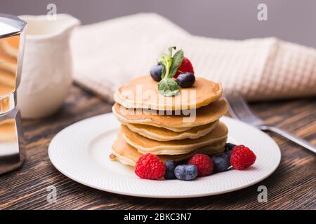 Pile de crêpes aux myrtilles et framboises pour le petit déjeuner sur table en bois. Banque D'Images