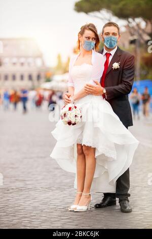 Couple récemment marié avec masque de visage le jour de leur mariage. Dans la rue avec le Colisée en arrière-plan à Rome, Italie. La mariée, dans un mer blanc Banque D'Images