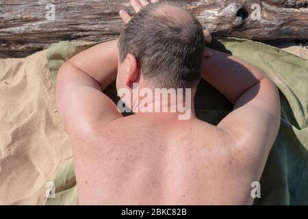 Homme soleil. Homme d'âge moyen allongé sur la plage à l'extérieur. Le soleil brille sur son corps. Banque D'Images