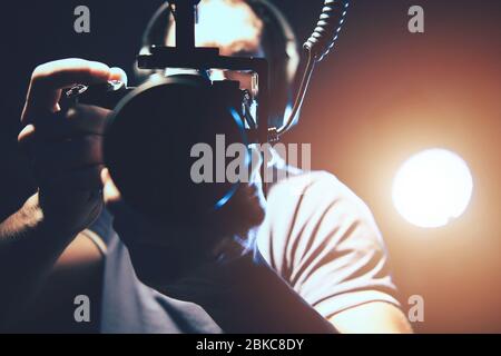 Vidéaste avec appareil photo reflex numérique professionnel en mains prenant des photos à main levée pour sa production vidéo documentaire. Spot LED pour éclairer la scène de Banque D'Images
