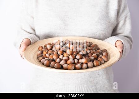 Femme tenant des noisettes décortiquées sur une assiette en bois. En-cas crus et sains. Noix non grillées et bio. Banque D'Images