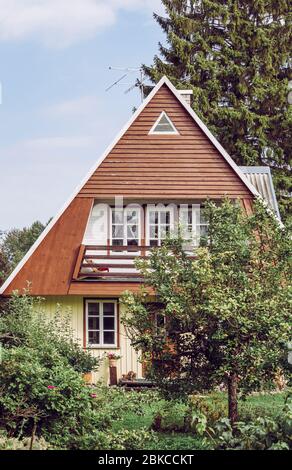 Jolie petite maison de campagne rétro avec jardin verdoyant et luxuriant le jour ensoleillé de l'été. Fenêtres avec grilles et murs en bois peints en jaune. Banque D'Images