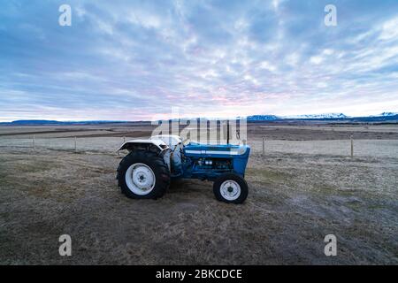 Photo du stock agricole. Un petit tracteur sur un champ pendant le coucher du soleil. Agriculture en Islande, Scandinavie. Photo d'arrière-plan d'un tracteur Banque D'Images