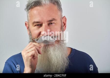 Portrait d'homme barbu mûr à poil gris en sweat-shirt bleu avec sabot de moustache sur fond gris, foyer sélectif Banque D'Images