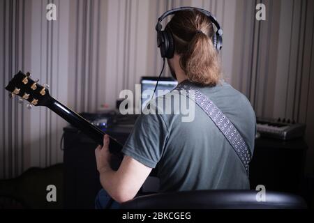 Homme barbu musicien jouant de la musique et composer une chanson avec piano électrique de guitare et ordinateur portable tout en s'assoir dans le salon, virus de la couronne Banque D'Images