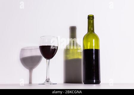 Un verre de vin et une bouteille jettent une longue ombre du soleil du soir. Banque D'Images