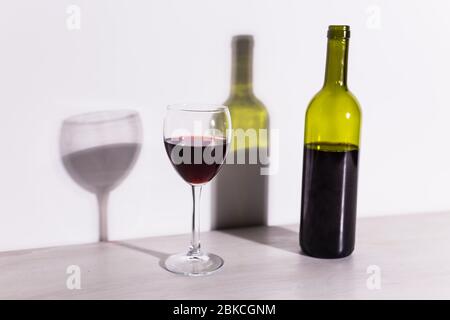 Un verre de vin et une bouteille jettent une longue ombre du soleil du soir. Banque D'Images