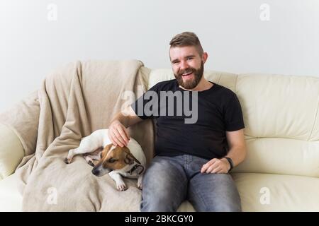 Attrayant gai caucasien mâle dans une chemise décontractée assis sur le canapé animal préféré. Joyeux barbu avec son Jack russell terrier. Propriétaire de l'animal Banque D'Images