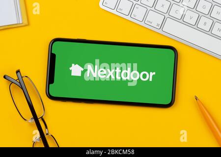 Un smartphone affichant le logo nextdoor repose sur un fond jaune avec un clavier, des lunettes, un stylo et un livre (usage éditorial uniquement). Banque D'Images