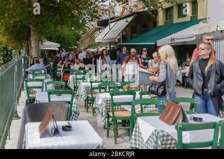 Athènes, Grèce, se foule autour de tables de restaurant à moitié vides. Monastiraki avec des touristes le long de la taverne extérieur coin salon avec des chaises vertes en bois. Banque D'Images