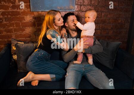 La petite fille drôle touche le visage du père tandis que la mère regarde Banque D'Images