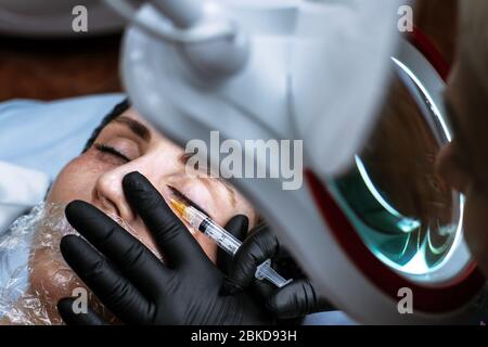 Esthéticienne fait une injection de beauté. Le médecin injecte une injection sous les yeux d'une jeune femme. Services de cosmologiste. Banque D'Images