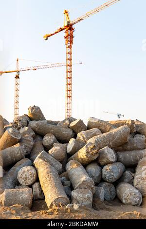 Grande pile de pieux de béton taillé sur le chantier, grues de tour sur fond. Banque D'Images