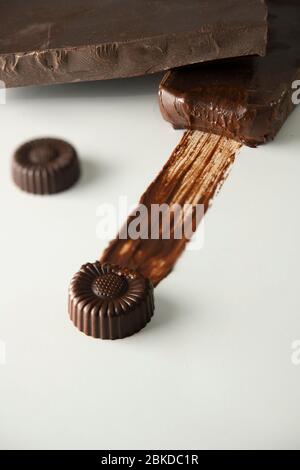 Petits chocolats sur fond blanc et gros morceaux d'un chocolat noir Banque D'Images
