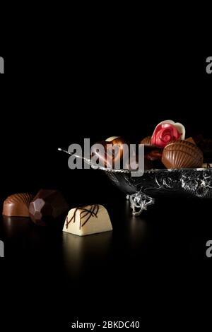 Différents petits chocolats dans une plaque argent avec fond noir Banque D'Images