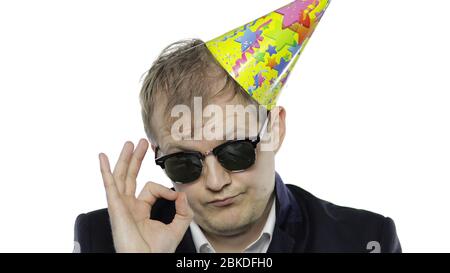 Portrait de l'homme jeune et endormi de la planche avec un hangover montrant le signe OK. Émotions. Homme d'affaires en costume avec bouée, casquette festive et lunettes de soleil. Fond blanc. Concept de fête d'anniversaire de bureau Banque D'Images