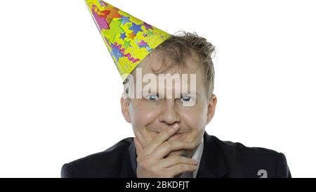 Portrait de l'homme jeune et endormi de la planche avec un sourire de gueule. Émotions. Un homme d'affaires en costume et un bonnet festif à la vaisselle regarde l'appareil photo. Fond blanc. Concept de fête d'anniversaire de bureau Banque D'Images