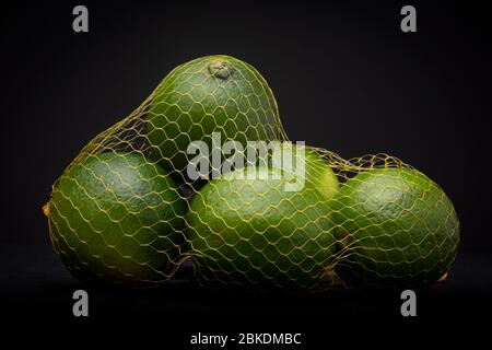Fruits vert vif à la chaux fraîche dans un sac à filet de gaze contrasté sur un fond gris foncé. Studio produit clé faible durée de vie. Banque D'Images