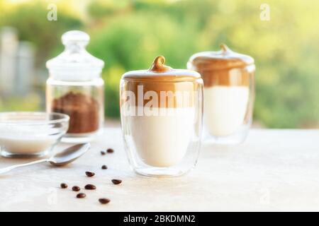 Délicieux café Dalgona maison dans une tasse en verre avec des ingrédients, du café et du suger sur une table sur fond vert. Recette populaire de la Corée boire latte avec f Banque D'Images