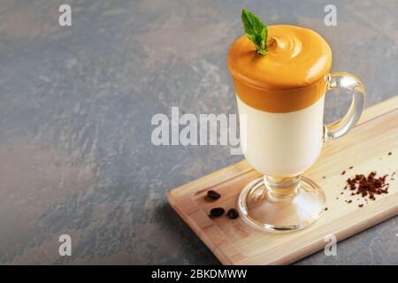 Café Dalgona maison dans une tasse en verre sur planche en bois sur fond gris. Tendance café à latte glacé coréen avec mousse de café instantané avec café Banque D'Images