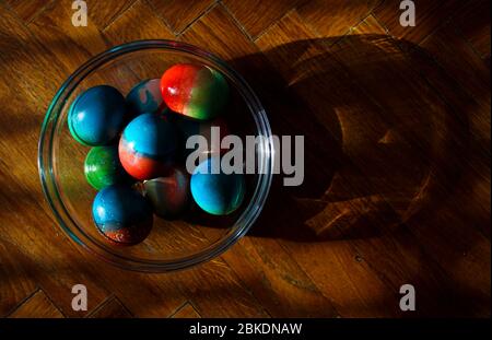 Œufs aux couleurs vives pour Pâques dans un bol en verre sur le sol de la parquette Banque D'Images