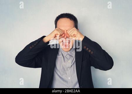 Homme d'affaires criant et pleurant couvrant ses yeux avec ses mains sur fond bleu. Perte d'argent. Faillite de pe réussi Banque D'Images