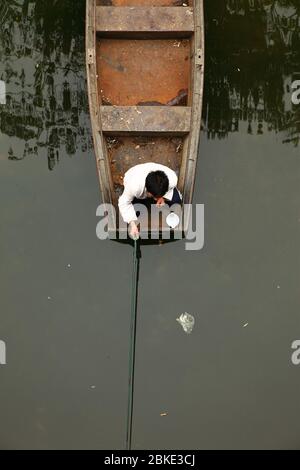 Vue verticale aérienne d'un homme accroupi sur le bord de son bateau rouillé en train de pêcher, Pékin, Chine Banque D'Images