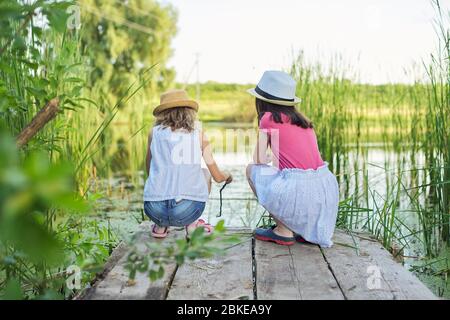 Filles enfants sur la jetée en bois du lac dans les roseaux, jouant avec l'eau, parlant Banque D'Images