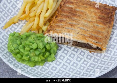 Steak et tarte aux oignons avec frites et petits pois. Sur une nappe grise de chiné Banque D'Images