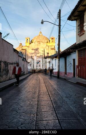 Vue sur la cathédrale de San Cristobal de las Casas illuminée par le soleil tôt le matin à travers une allée pavée vide. Banque D'Images