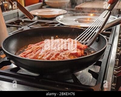 Un chef cuisinra des crêpes okonomiyaki traditionnelles dans une huile chaude dans une casserole. Le mélange de crêpes japonaises est retourné pour voir le dessous doré. Banque D'Images