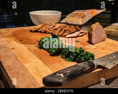 Gros plan sur une planche à découper avec des ingrédients de Ramen. Des épinards et du porc hachés sont visibles dans la partie avant du sol et dans un couteau de cuisine. Banque D'Images