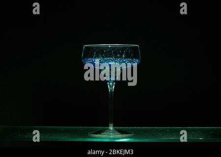 Verre à cocktail de style martini unique, affichage lumineux avec caviar bleu dans le style d'un cocktail. Verrerie d'art avec eau colorée Banque D'Images